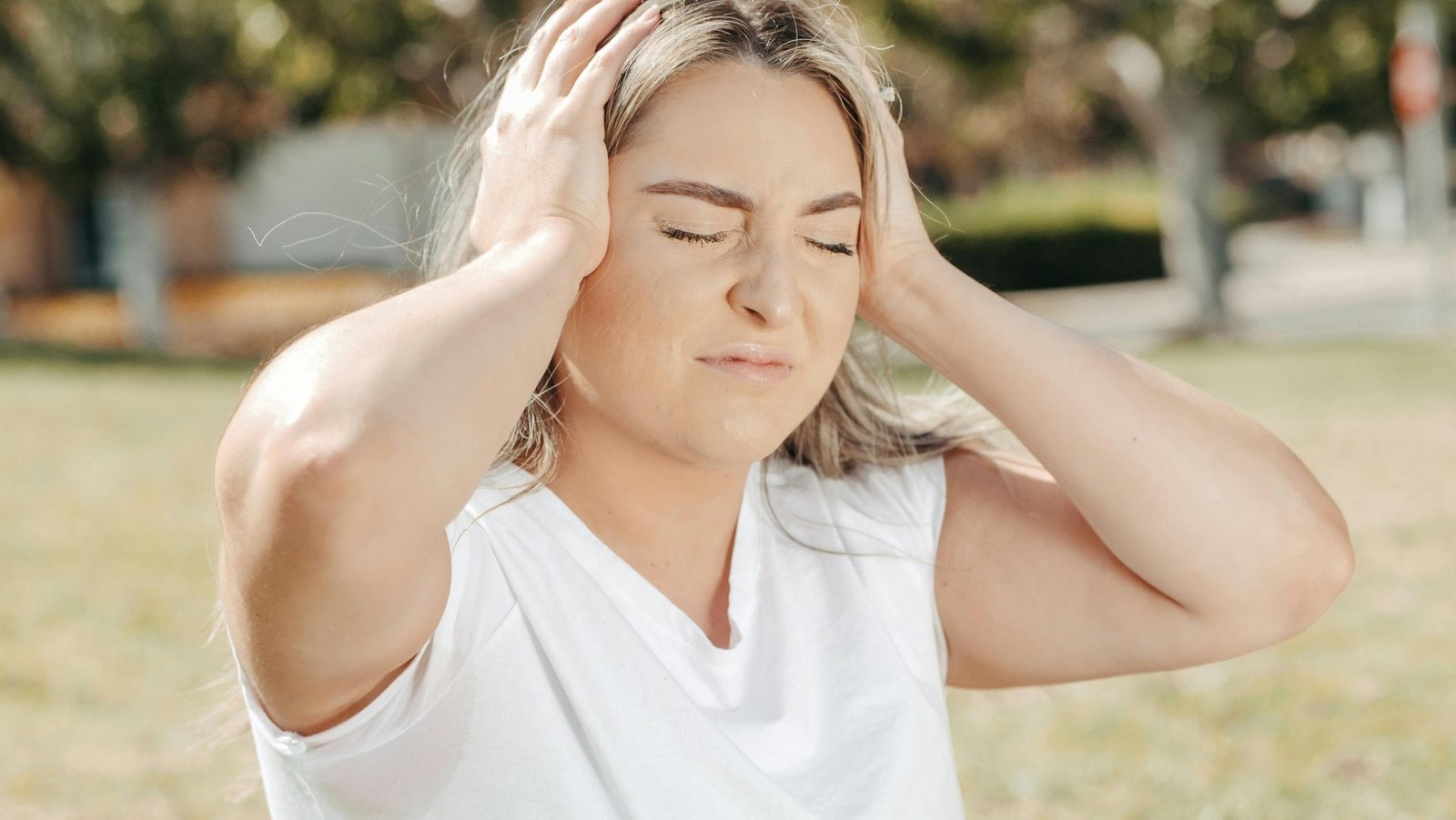 A woman outdoors holds her head, depicting stress or a headache.